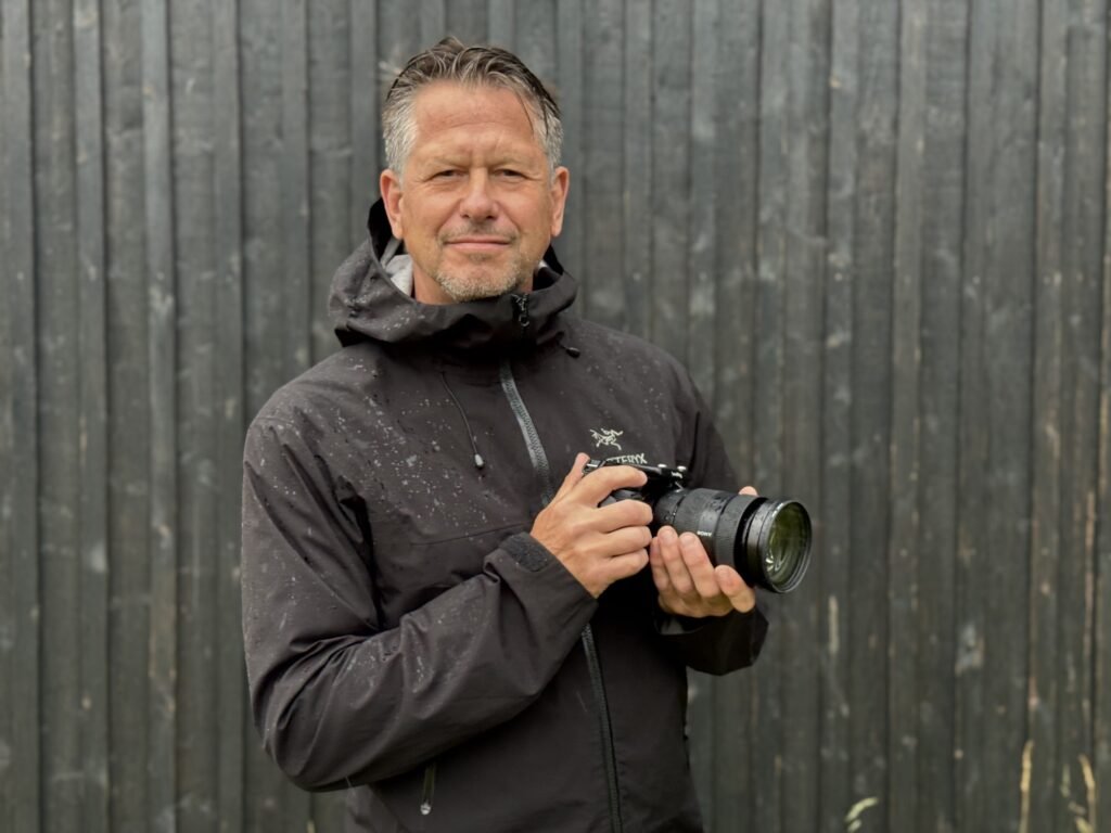 Jacob Bjelfvenstam, stills photographer, holding his camera in front of a black wooden wall in Stockholm