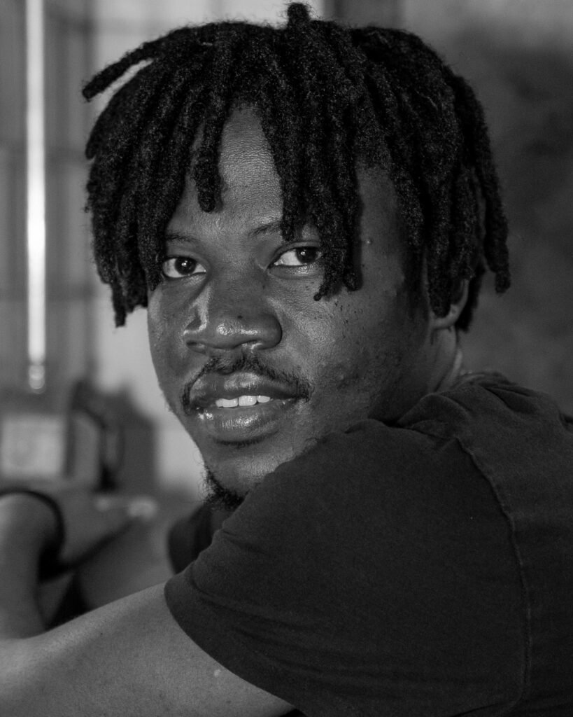 Black and white portrait of a man with shoulder-length locs looking back over his shoulder