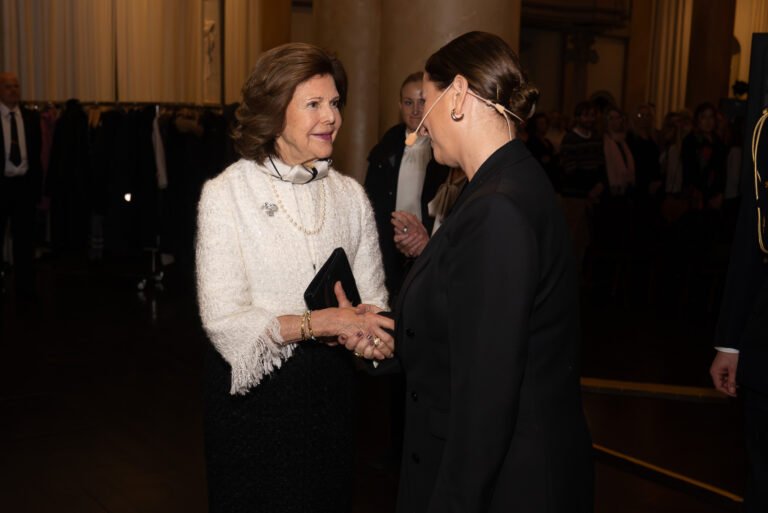 Two women in conversation at a formal evening reception in a grand, warmly lit hall