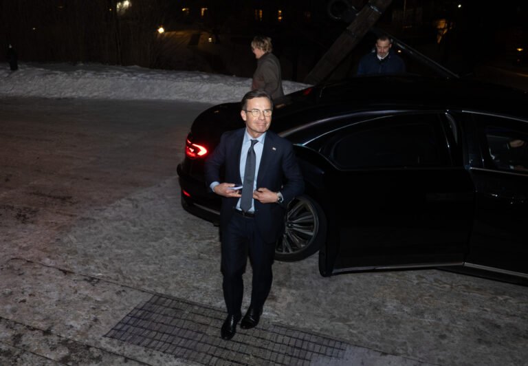 Man in a dark suit stepping out of a black car on a snowy evening at the entrance to an event
